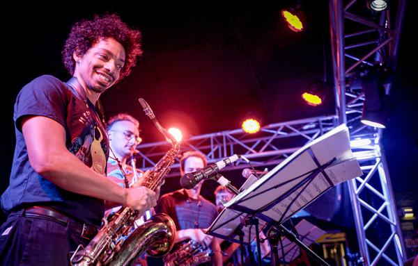 Bandfoto Noisy Neighbours Dance Party: Bläser auf Bühne bei Live-Konzert Mehrere Musiker stehen auf einer Bühne und spielen Blasinstrumente während eines Live-Konzerts. Im Vordergrund spielt eine Person mit lockigem Haar ein Saxofon und lächelt dabei. Wei